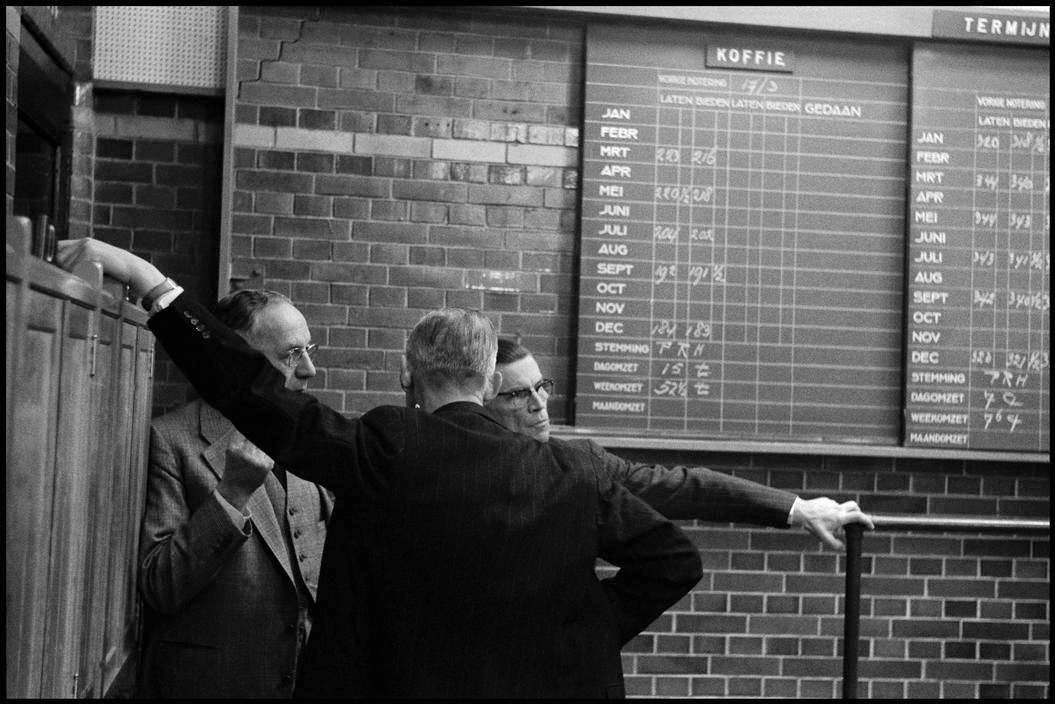 Varios hombres en la bolsa de Amsterdam entre los 50 y los 60. Estan frente a una pared y las cotizaciones esetán escritas con tiza en una pizarra ordenada. © Leonard Freed/Magnum Photos